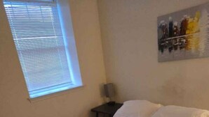 A bedroom with a bed, a nightstand, a lamp, a window with blinds, and a painting on the wall. - 1BR/1BA Comfortable & Convenient (Belleville)