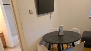 A room with a round table, four chairs, a flat-screen TV mounted on the wall, and a white door leading to another room. - 1BR/1BA Comfortable & Convenient (Belleville)