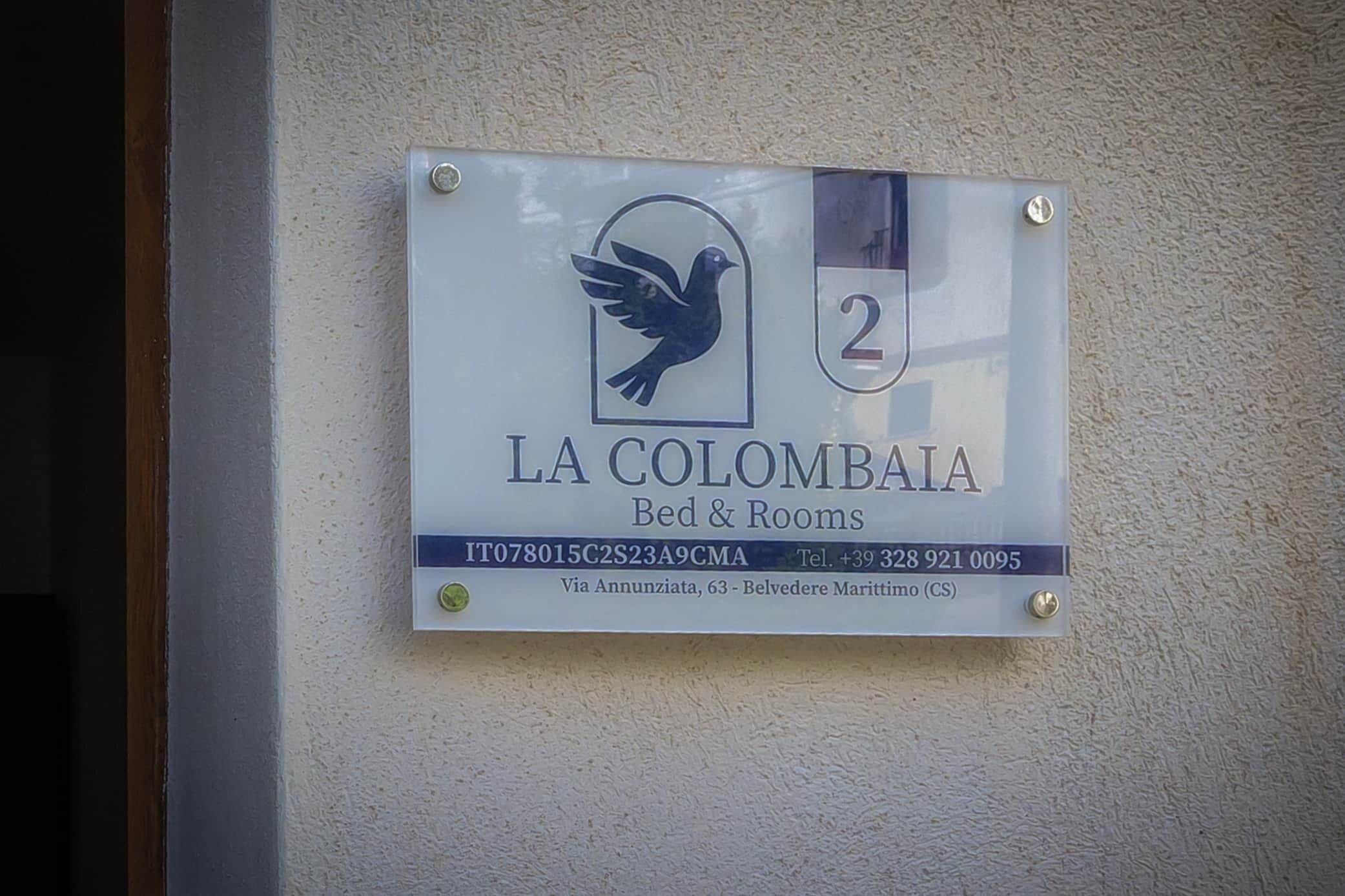 Une enseigne pour « LA COLOMBIA Bed & Rooms », avec un logo représentant un oiseau, le numéro de chambre (2) et les coordonnées.