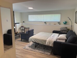A bedroom with a bed, a sofa, a chair, a small table, a globe, and a window with blinds.