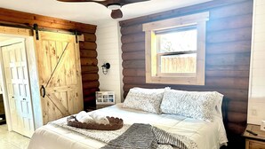 Ein Schlafzimmer in einer Blockhütte mit Bett, Deckenventilator, Fenster und Holztür.