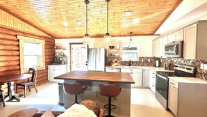 Eine geräumige Küche mit Holzbalken, einer zentralen Kochinsel mit Sitzgelegenheiten und modernen Geräten.
