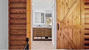 Ein Holzinnenraum mit einer Schiebetür im Bauernhausstil, die zu einem Badezimmer mit Spiegel, Waschbecken und Holzwaschtisch führt.