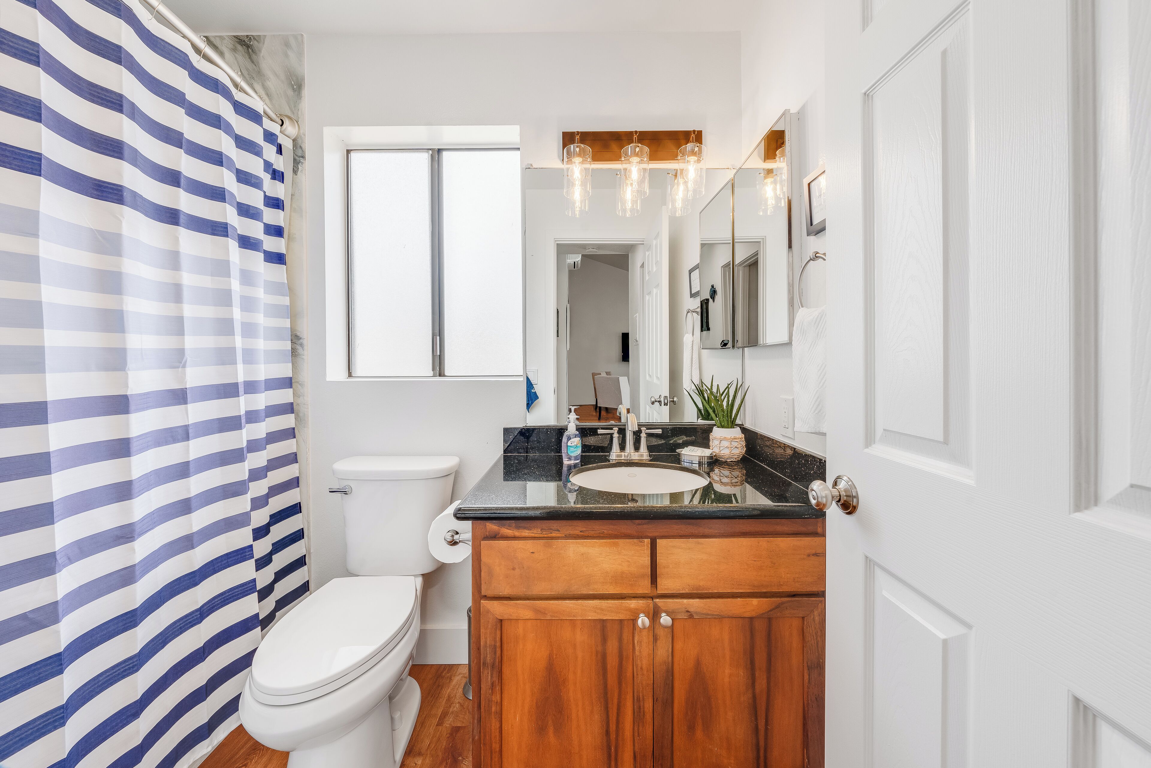Une salle de bain avec un rideau de douche à rayures, des toilettes, un lavabo avec un meuble-vasque en bois et un miroir au-dessus du lavabo.
