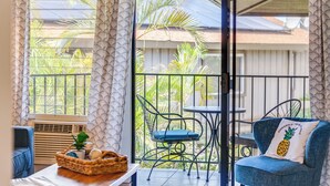 A balcony with a wicker basket, a blue chair, and a table with a pineapple pillow. - Sleeps 12! Ocean Views! 4 BD/4BA! 2 Renovated Condos! (Kihei)