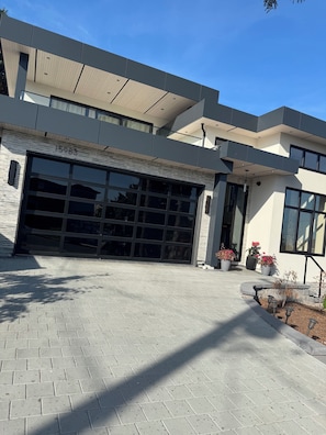 A modern two-story building with a large garage door, brick paving, and potted plants. - Cozy two bedroom Suite (White Rock)