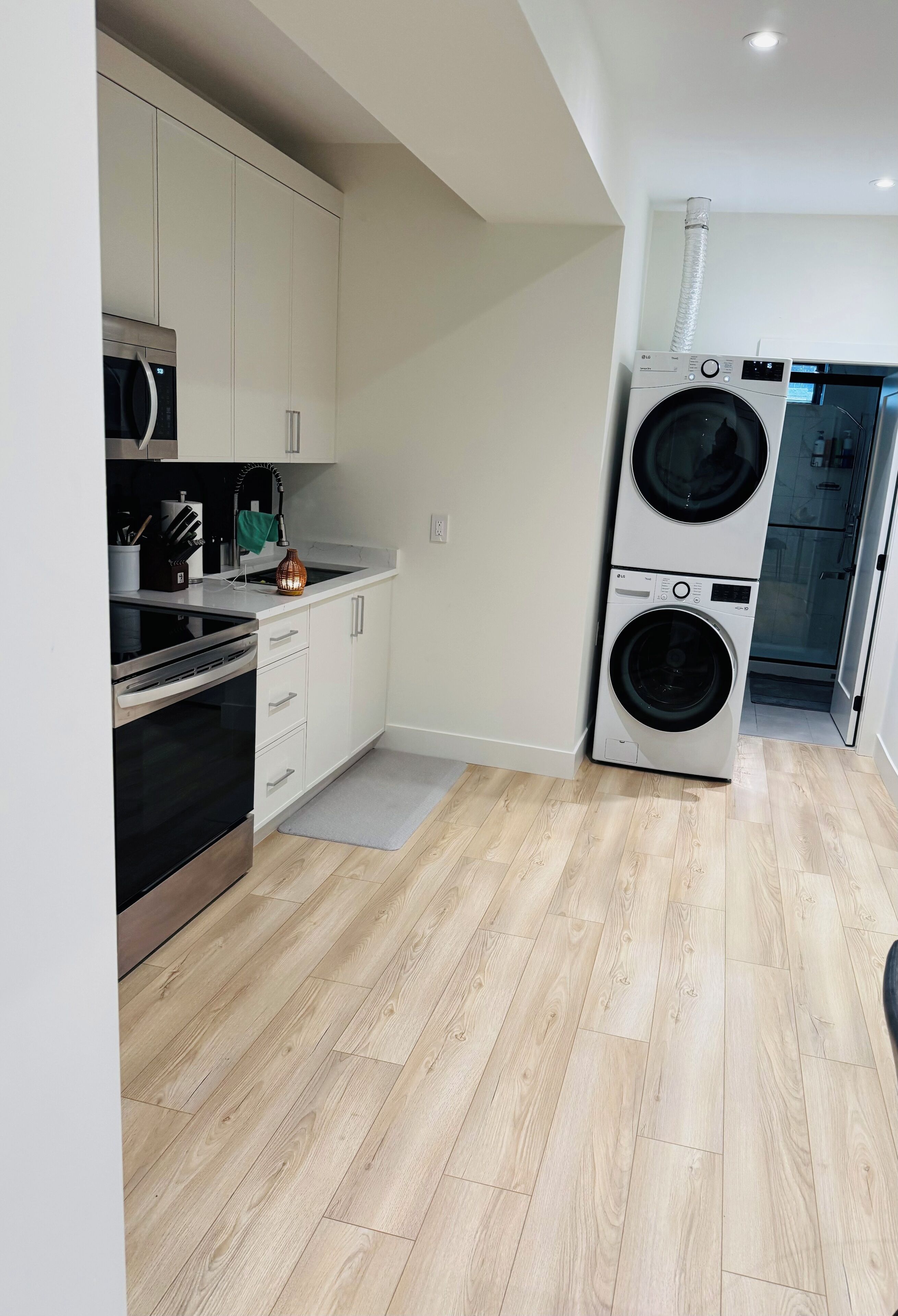 Une cuisine moderne avec des meubles blancs, un four en acier inoxydable et un lave-linge à deux tambours.