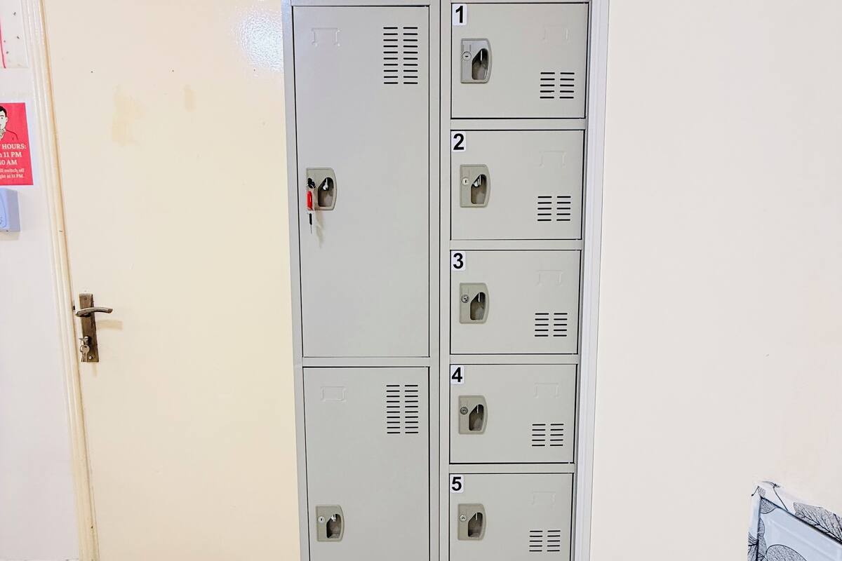 A row of six numbered lockers in a hallway with a door on the left and a poster on the right.