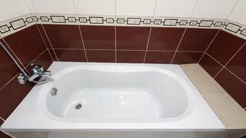 Une baignoire rectangulaire dotée d’un robinet et d’un drain en chrome, placée devant un mur recouvert de carreaux bruns et beiges, le tout agrémenté d’une bordure décorative.