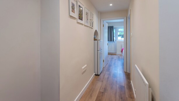 Un pasillo estrecho con piso de madera, paredes blancas y una puerta que da a una habitación con ventana.