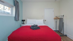 Un dormitorio con cama, mesita de noche, ventana con cortinas, puerta y perchero con abrigo.