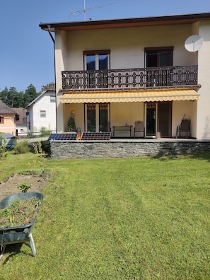 A two-story house with a balcony, a stone wall, and a grassy yard.