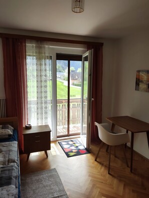 A bedroom with a bed, a wooden nightstand, a desk, and a chair. There is a sliding glass door leading to a balcony with a view of a green landscape. - Variety of lakes: Klopeiner See, Gösselsdorfer See, Turner See. (Sittersdorf)