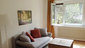 A modern living room with a grey sofa, a wooden coffee table, and a white armchair. A painting is on the wall, and a window with curtains is visible. - Variety of lakes: Klopeiner See, Gösselsdorfer See, Turner See. (Sittersdorf)