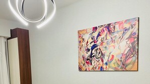 Ein gelbes Sofa mit Kissen, eine moderne Leuchte und ein farbenfrohes abstraktes Gemälde an der Wand.