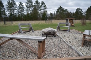 A wooden deck with two benches and a table, surrounded by gravel and a grassy area with trees in the background. - Woodland Retreat with 40 acre and 4 Bedrooms Perfect for Families & Dogs (Mauston)