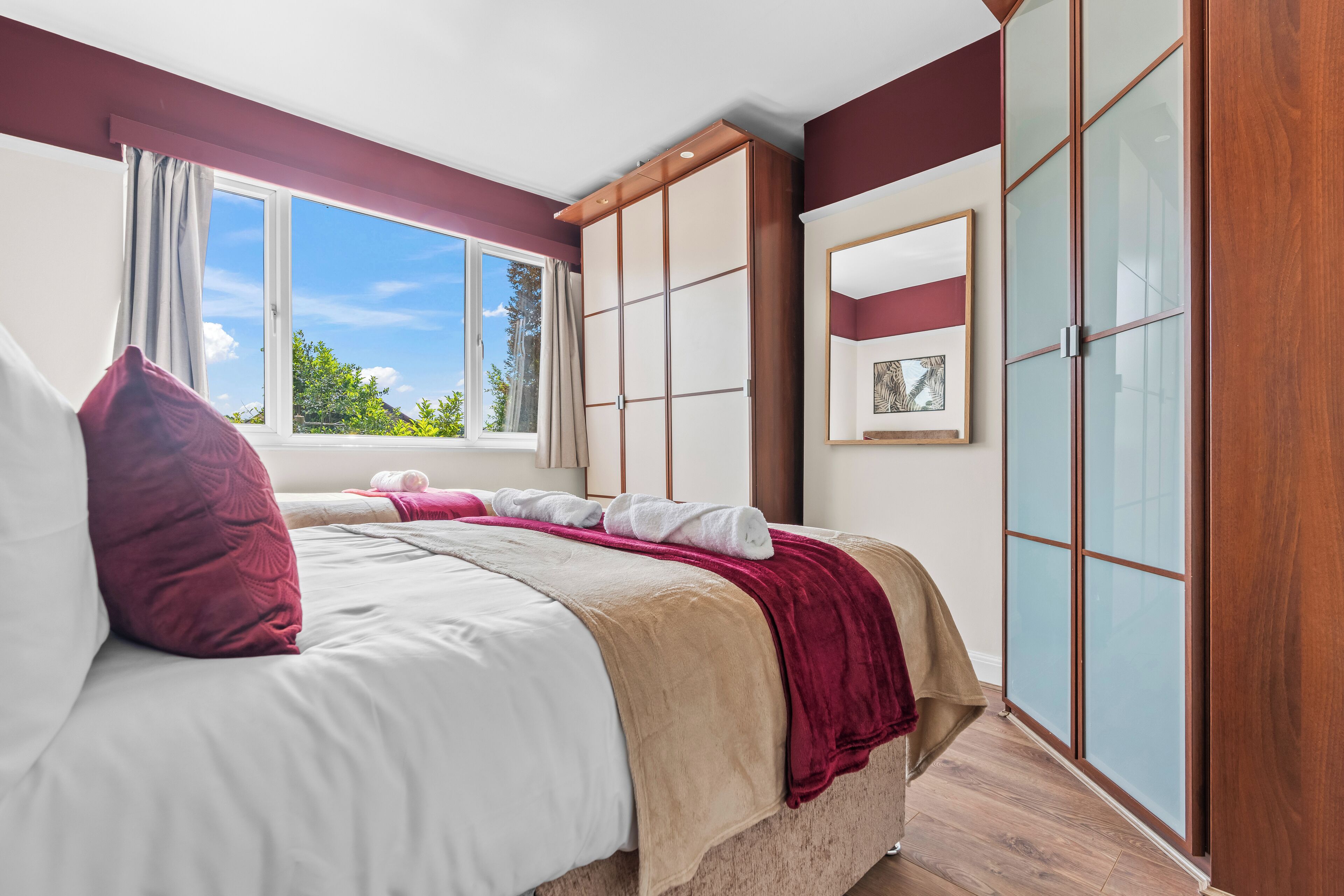A bedroom with a large bed, a wardrobe, and a window with a view of greenery.