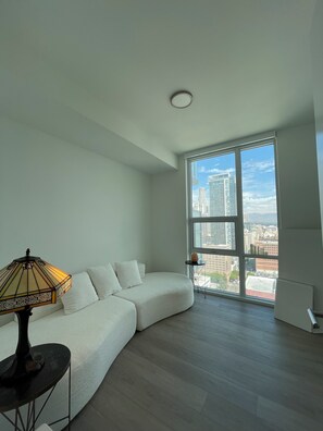 A modern living room with a large window, a white sofa, a small table, and a floor lamp. - Influencer views in the heart of DTLA (Los Angeles)