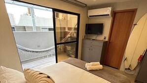 A modern hotel room with a large bed, a TV, an air conditioning unit, and a surfboard. - Melhores Flats - Espaçoso pé na areia (João Pessoa)