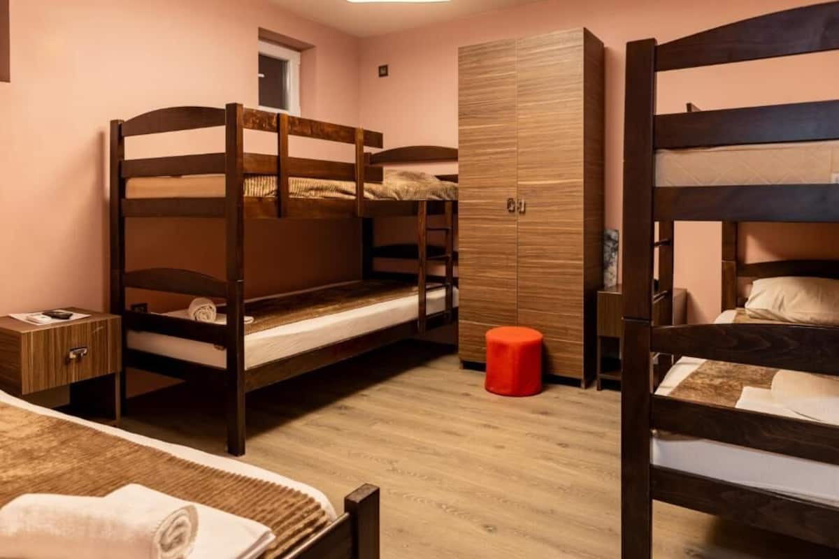Ein Zimmer mit Etagenbetten, einem Kleiderschrank, einem kleinen Hocker und einem Nachttisch mit Lampe.