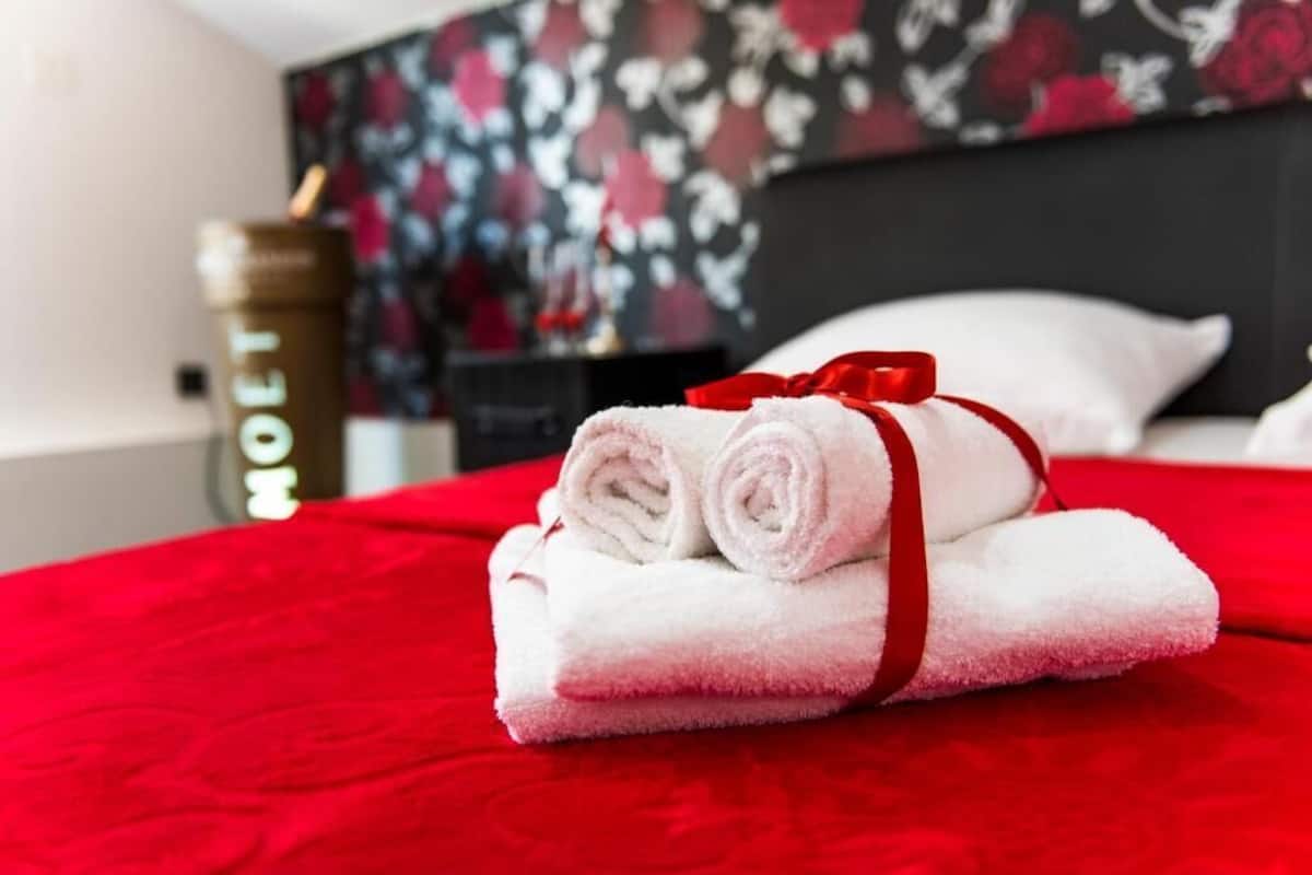 Ein ordentlich bezogenes Bett mit roter Bettwäsche und weißen Handtüchern, verbunden mit einer roten Schleife.