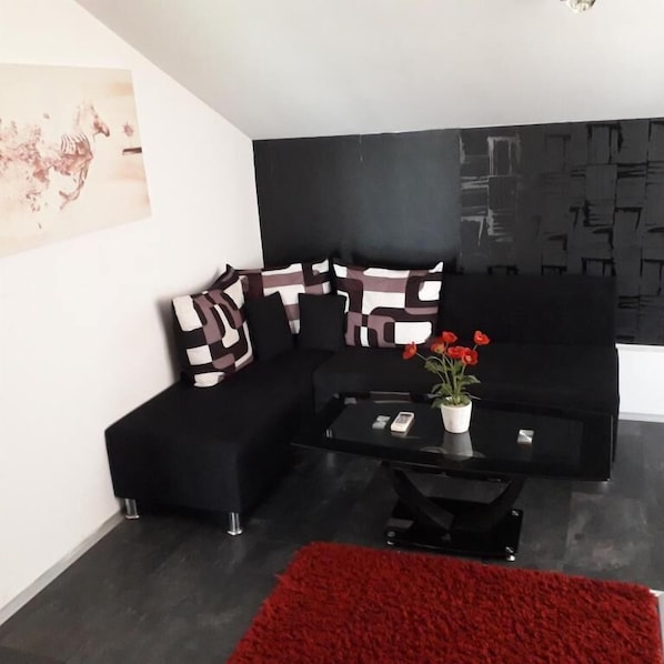A modern living room with a black sofa, patterned cushions, a glass coffee table, and a red rug.