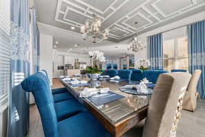Un espace repas moderne avec une table à plateau en verre, des chaises recouvertes d’un tissu bleu et un lustre.