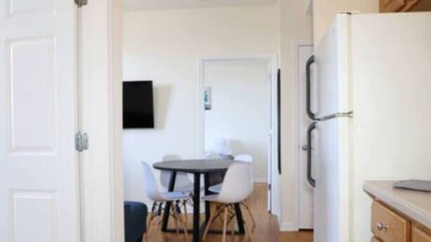 A room with a dining table and chairs, a white door, and a refrigerator. - Stylish 1BR Apartment Prime Location (Belleville)