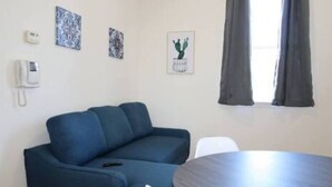 A room with a blue sofa, a small table, a phone, and a window with curtains. - Stylish 1BR Apartment Prime Location (Belleville)