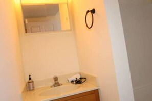 Un baño con lavamanos blanco, un espejo, un aro para toallas y una botella de jabón de manos.