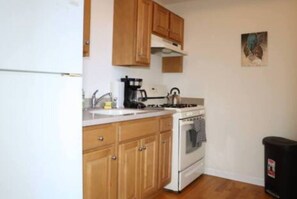 Cocina compacta con armarios de madera, estufa y cafetera.
