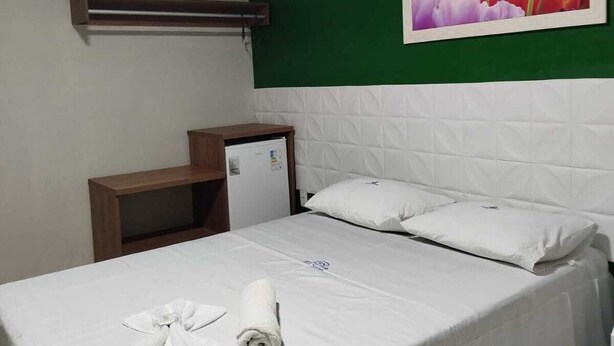 Habitación de hotel con cama, escritorio pequeño, refrigerador y pared verde con un cuadro de flores.