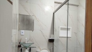 A modern bathroom with a toilet, glass shower enclosure, and a small sink. - HOTEL NOVAES (Castanhal)