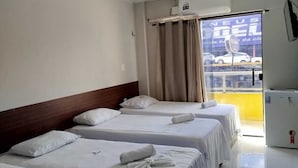 Habitación de hotel con tres camas, ventilador de techo, ventana con cortinas y vista al exterior.