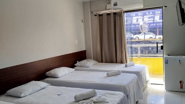 A hotel room with three beds, a ceiling fan, a window with curtains, and a view of the outside. - HOTEL NOVAES (Castanhal)