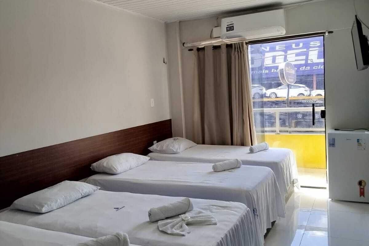 A hotel room with three beds, a ceiling fan, a window with curtains, and a view of the outside.
