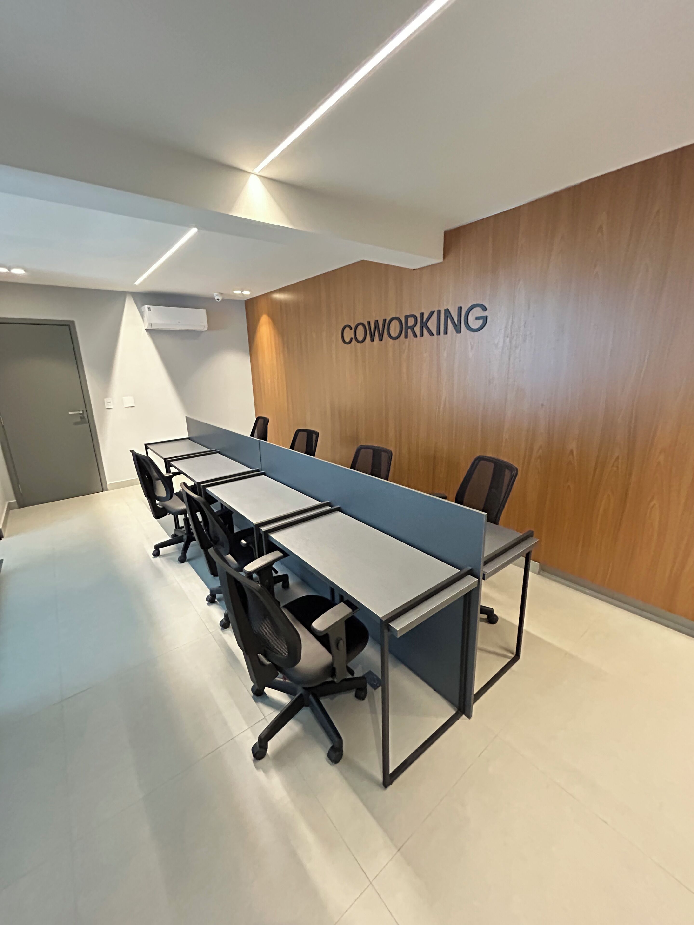 A modern coworking space with a long table, chairs, and a wooden accent wall with the word "COWORKING" on it.