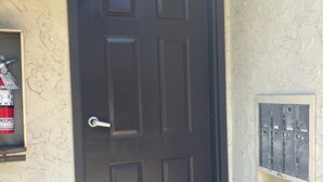 Una porta marró fosc amb un felp de porta que diu 'WELCOME' i una finestra petita amb marc metàl·lic.