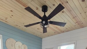 Une chambre avec un lit en bois, un ventilateur de plafond, une fenêtre avec des stores et un élément décoratif mural.