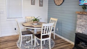 Un coin repas avec un plafond en bois, une table ronde entourée de chaises, une horloge au mur et un téléviseur diffusant une chaîne d’information.