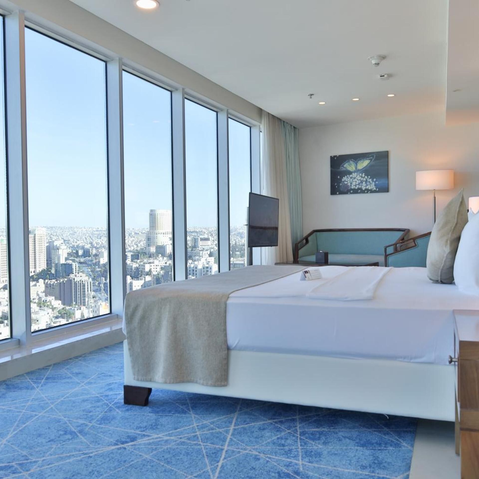 Habitación de hotel con una cama grande, vistas a la ciudad, un televisor de pantalla plana y un cuadro en la pared.