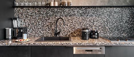 A kitchen with a granite countertop, a black faucet, a coffee maker, and a kettle.