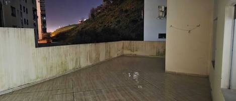Un balcon spacieux offrant une vue sur une colline et des bâtiments éloignés.