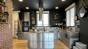 A modern kitchen with a central island, stainless steel appliances, and a brick accent wall. - Beautiful atypical loft with Jacuzzi (Tarascon)