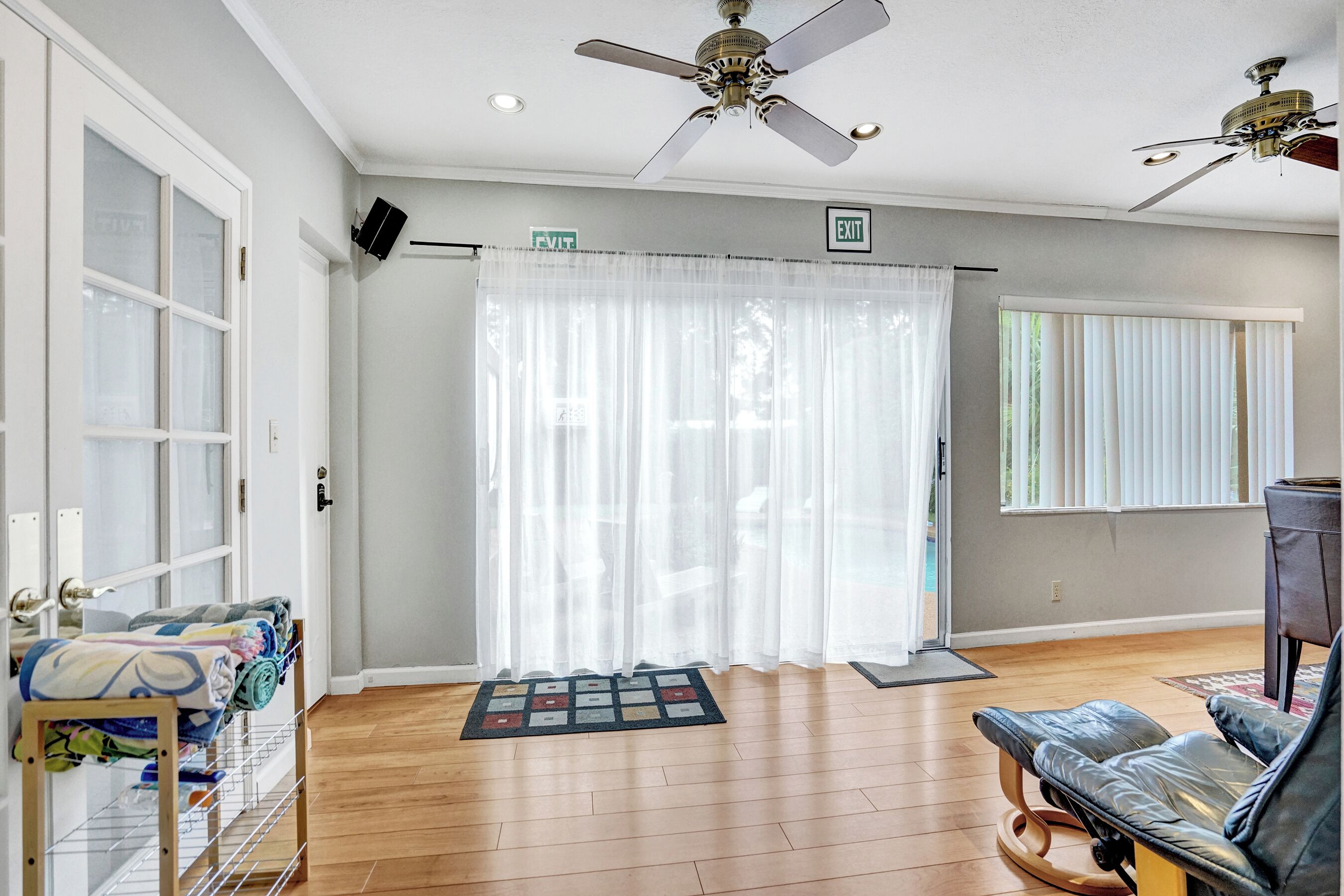 A spacious room with a wooden floor, a ceiling fan, a black leather chair, and a large window with blinds.