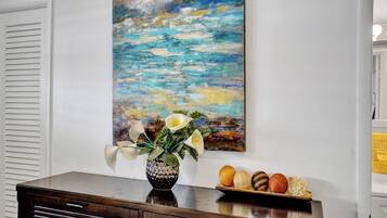 A room with a wooden dresser, a painting of a blue landscape, and a vase with flowers and fruits on the dresser.
