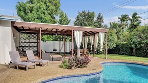 Une piscine dotée d’un patio couvert, de chaises longues et d’un petit jardin.