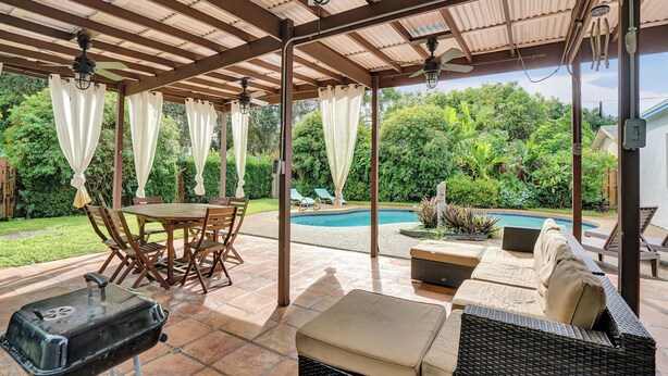 Un patio couvert avec une piscine, du mobilier d’extérieur et un barbecue.