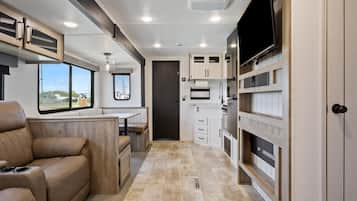 A compact RV interior with a kitchenette, seating area, and a TV mounted on the wall.