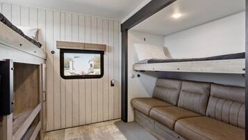 A compact interior with a bunk bed, a sofa, and a small window.